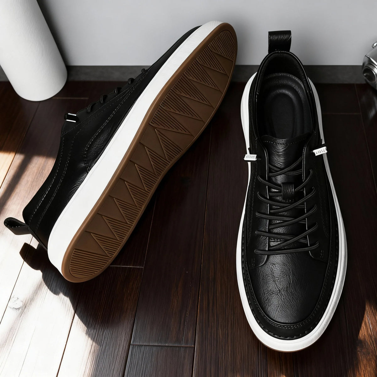 Overhead view of one black trainer on its side revealing gum tread pattern next to a second shoe shown upright