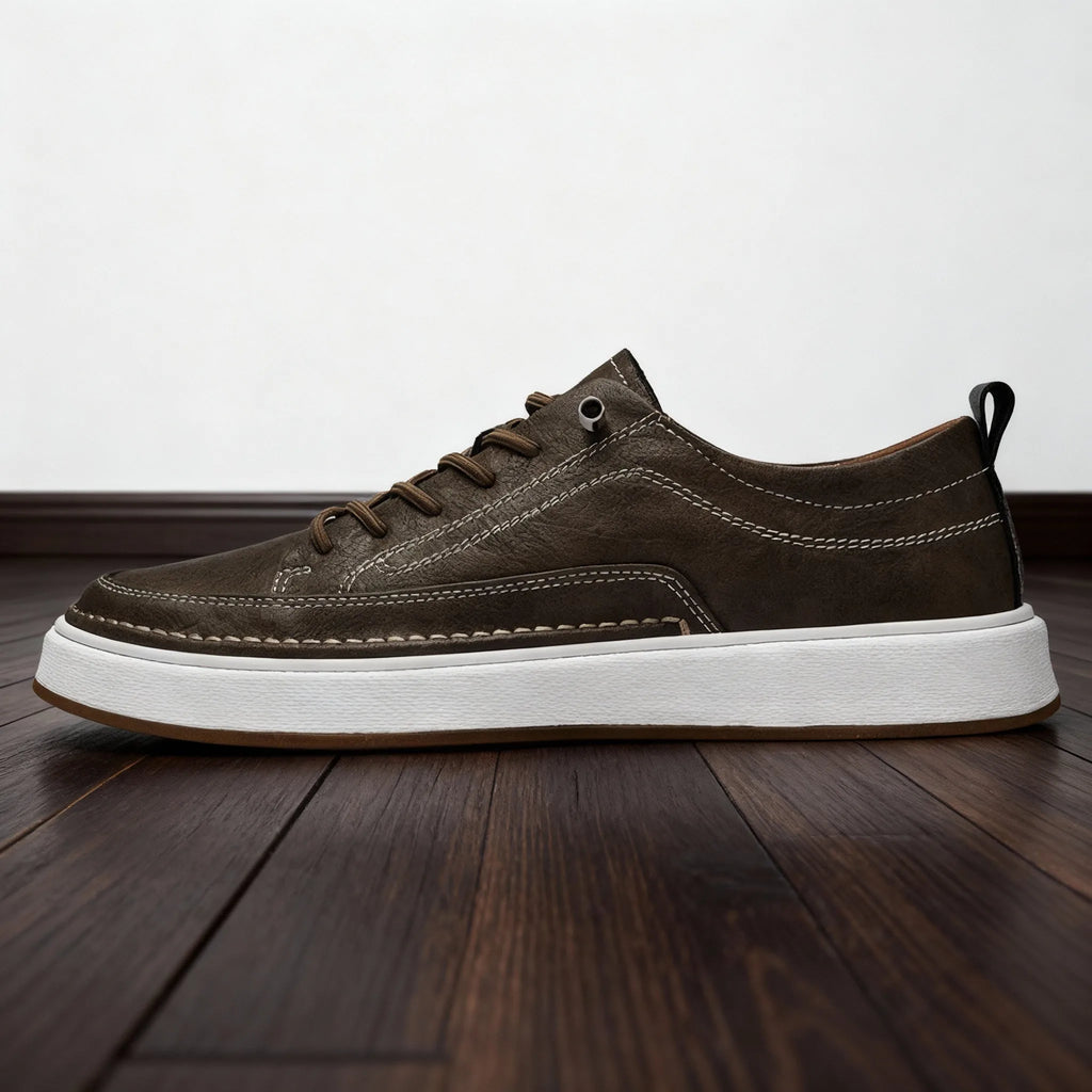 Full side profile of khaki brown leather trainer on wooden floor highlighting hand-stitched seams and pull tab
