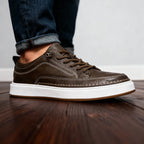 Close-up of khaki brown leather trainer worn on foot with rolled jeans, highlighting stitched vamp and cushioned sole