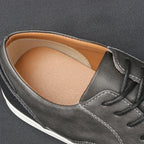 Front view of grey leather lace-up trainer showing rounded toe, eyelets and contrast stitching on dark background