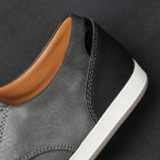 Close-up angle of navy leather trainer upper with tan trim and ribbed sole edge on wood surface