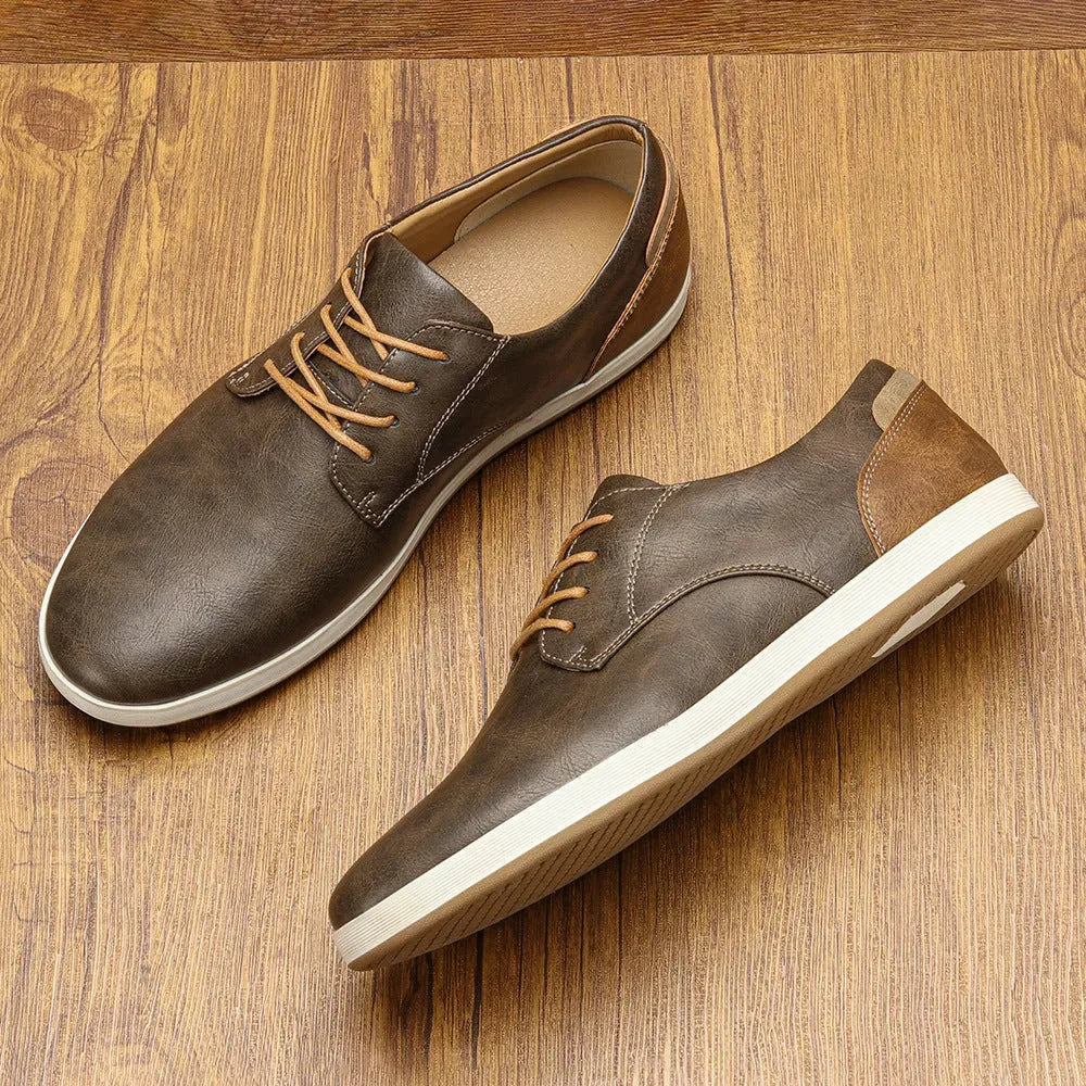 Pair of navy leather lace-up trainers on wood surface, one upright and one on its side showing ribbed sole