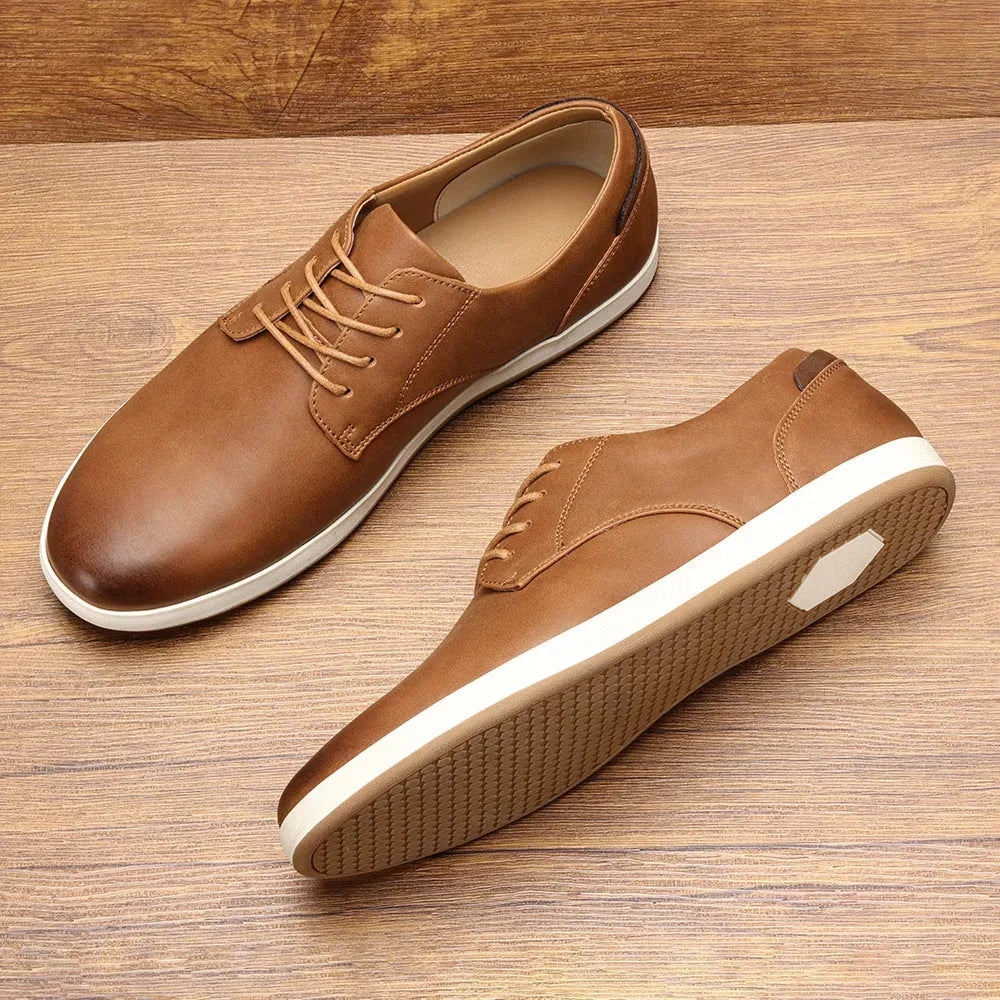 Pair of dark brown leather lace-up trainers with tan laces and heel patch resting on a wooden floor