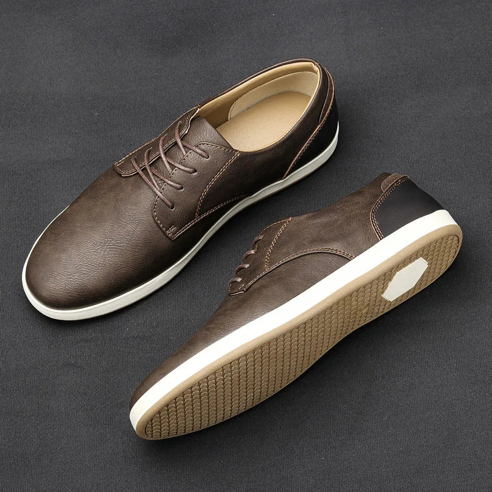 Pair of grey leather lace-up trainers with black heel and toe panels shown on a dark fabric background