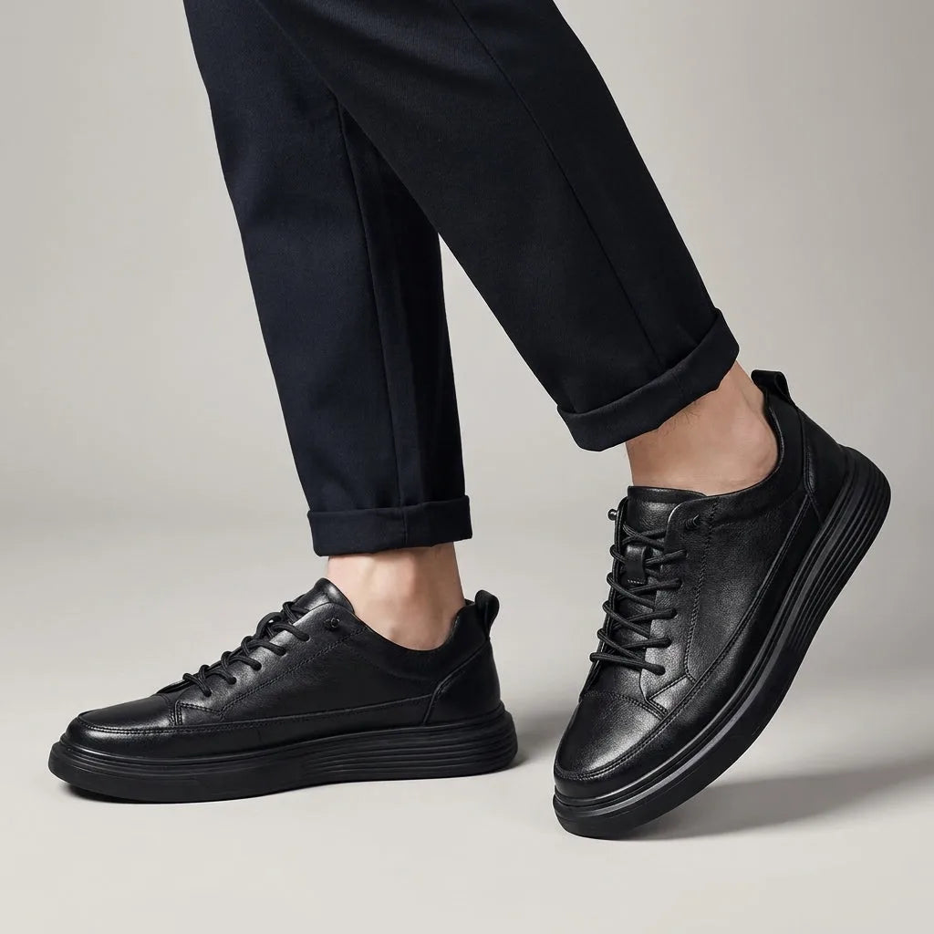 Side profile of a black leather lace-up trainer worn with tailored navy trousers rolled at the ankle