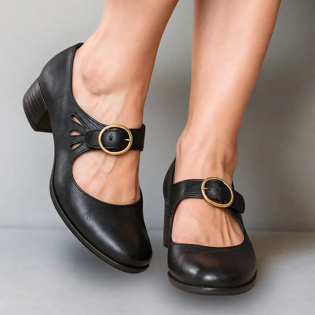 Close-up of black leather Mary Jane shoes with ankle strap, gold buckle and teardrop cut-out detail, worn on feet