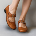 Tan brown leather Mary Jane pumps with silver buckle ankle strap and block heel, shown from above on model's feet