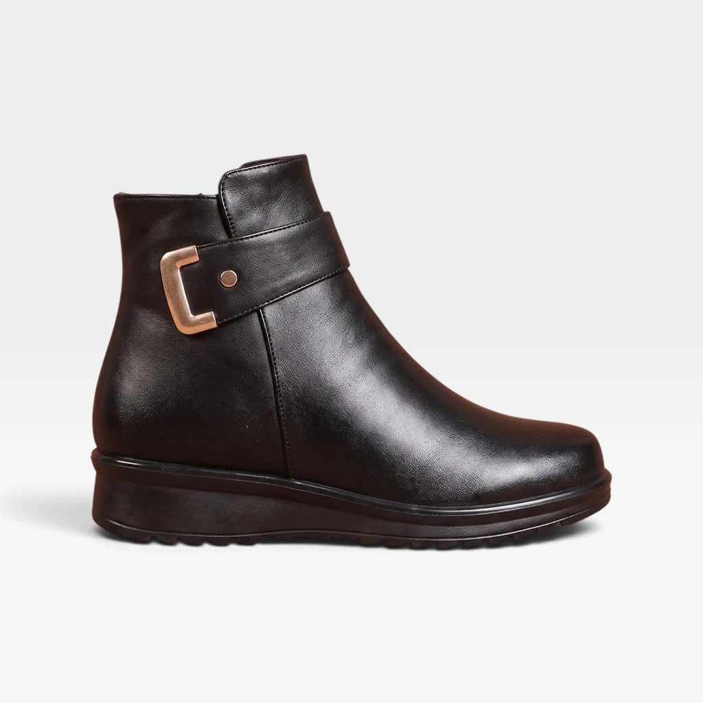 Side profile of black leather ankle boot with gold buckle strap and cushioned wedge sole against a plain backdrop