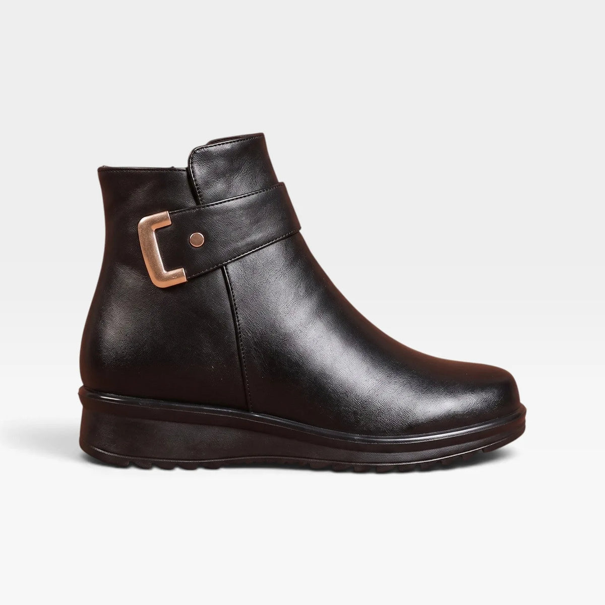 Side profile of black leather ankle boot with gold buckle strap and cushioned wedge sole against a plain backdrop