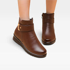 Close-up front view of brown leather ankle boots showing buckle strap, stitching detail and side zip