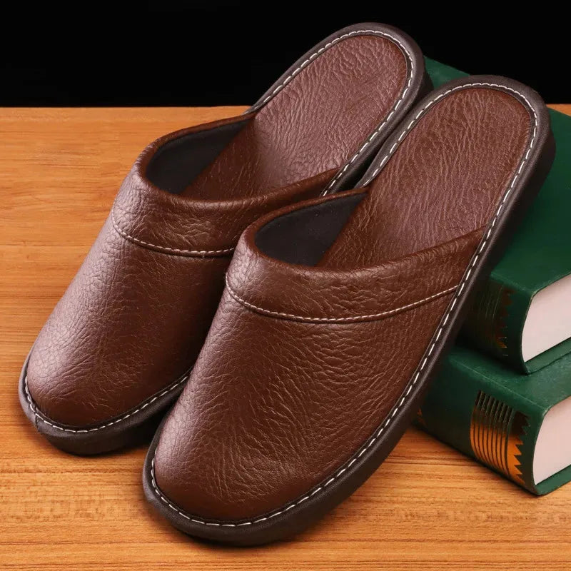 Pair of brown leather mule slippers with contrast stitching resting against green books on a wooden table