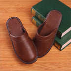 Top-down view of brown leather slip-on slippers angled beside stacked books on a wooden surface