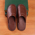 Overhead view of matching pair of brown leather slip-on slippers with white stitched trim