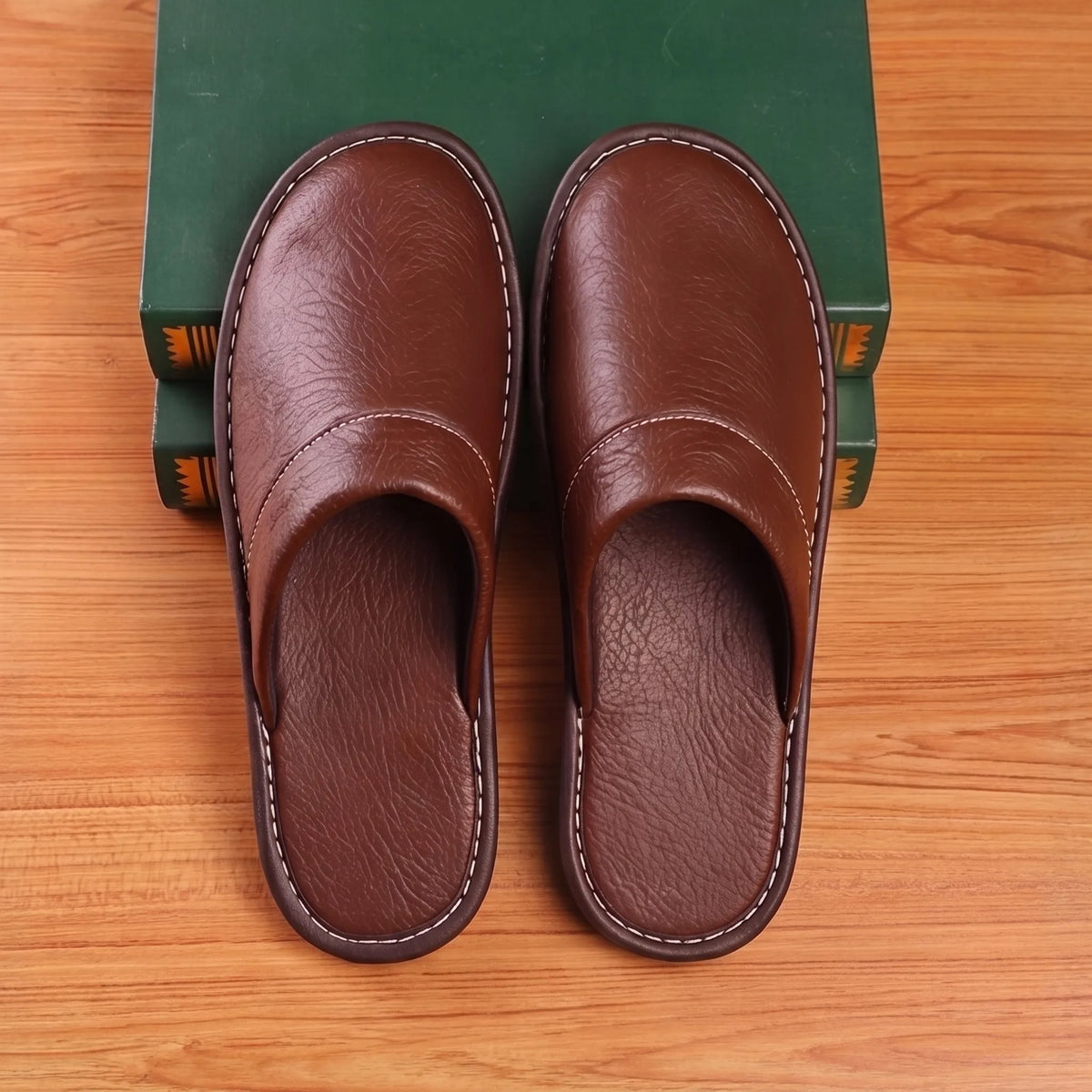Overhead view of matching pair of brown leather slip-on slippers with white stitched trim