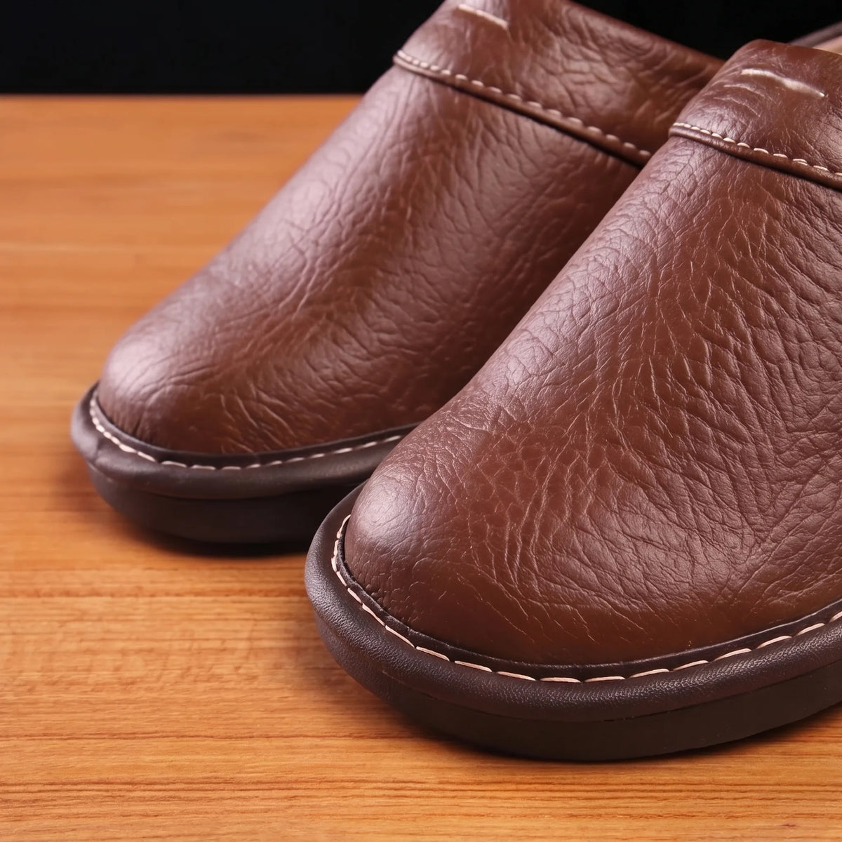 Close-up of textured brown leather upper showing visible grain and white stitched detailing