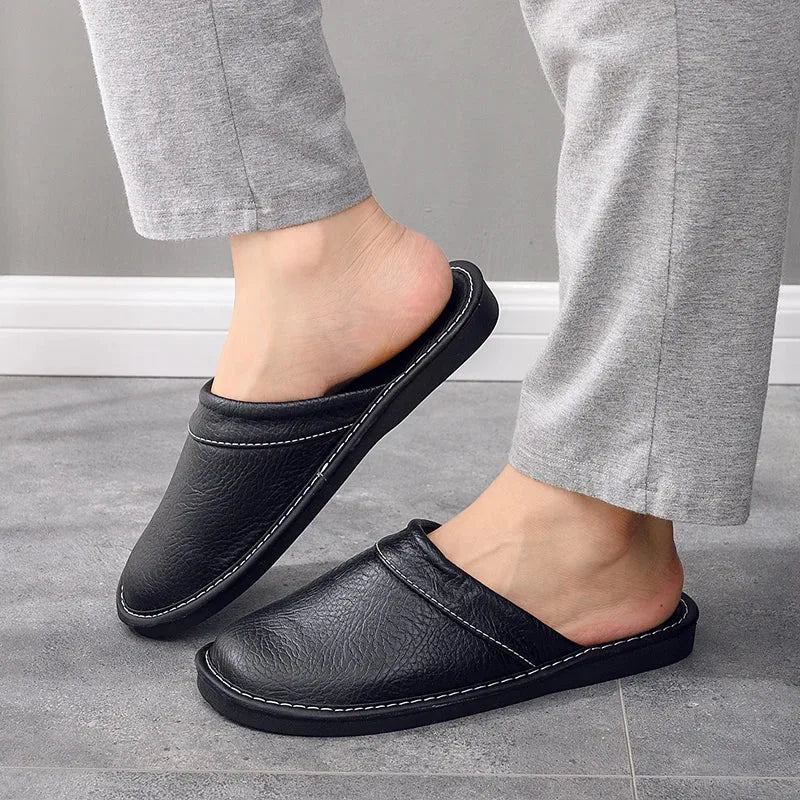 Side view of a foot wearing a black leather slip-on slipper with stitched trim, paired with trousers