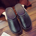 Overhead view of black leather slip-on slippers with white stitching held in hand on a wooden floor