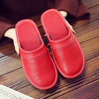 Overhead view of red leather slip-on slippers with white stitched trim held above a wooden floor