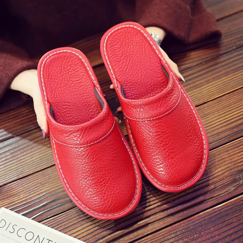 Overhead view of red leather slip-on slippers with white stitched trim held above a wooden floor