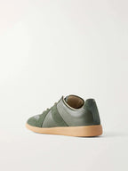 Three-quarter rear view showing the heel tab, suede panel detailing and gum sole of the green leather trainer