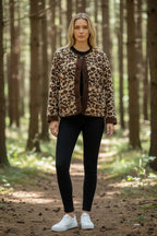 Woman standing in a forest wearing a leopard print fleece jacket with brown corduroy trim over black trousers and a black top.