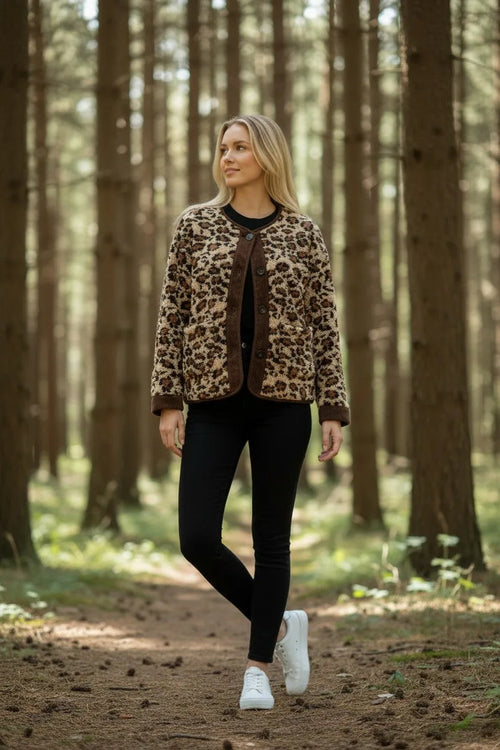 Woman walking along a woodland path wearing an open leopard print fleece jacket with white trainers and black jeans.