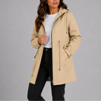 Model wears a beige lightweight hooded rain coat, unzipped over a white t-shirt, showing the drawstring waist and side pocket.
