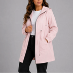 Pale pink hooded rain coat with drawstring waist cinched in, worn casually over black trousers.