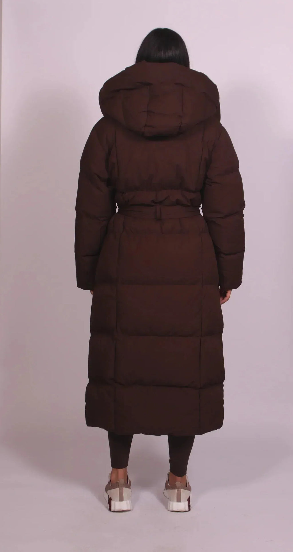 Back view of long brown puffer coat showing quilted panelling, hood and tied belt at the waist