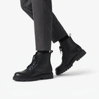 Model walking in black lace-up combat boots paired with grey tailored trousers and black socks