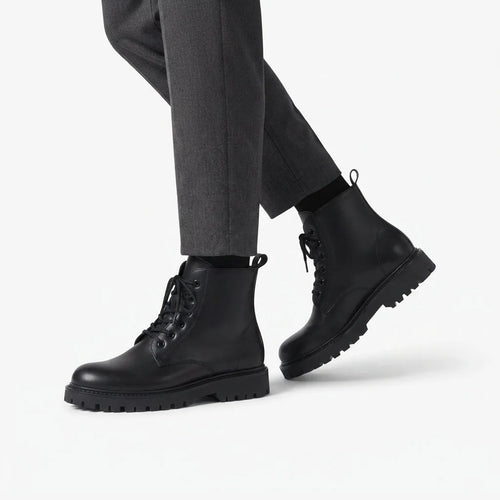 Model walking in black lace-up combat boots paired with grey tailored trousers and black socks