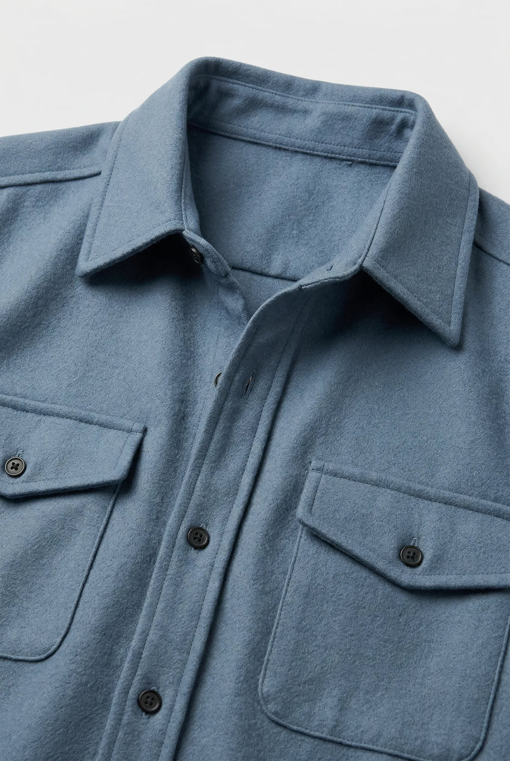 Close-up of the light blue overshirt fabric, collar and twin chest pockets with button flaps