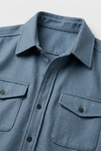Close-up of the light blue overshirt fabric, collar and twin chest pockets with button flaps