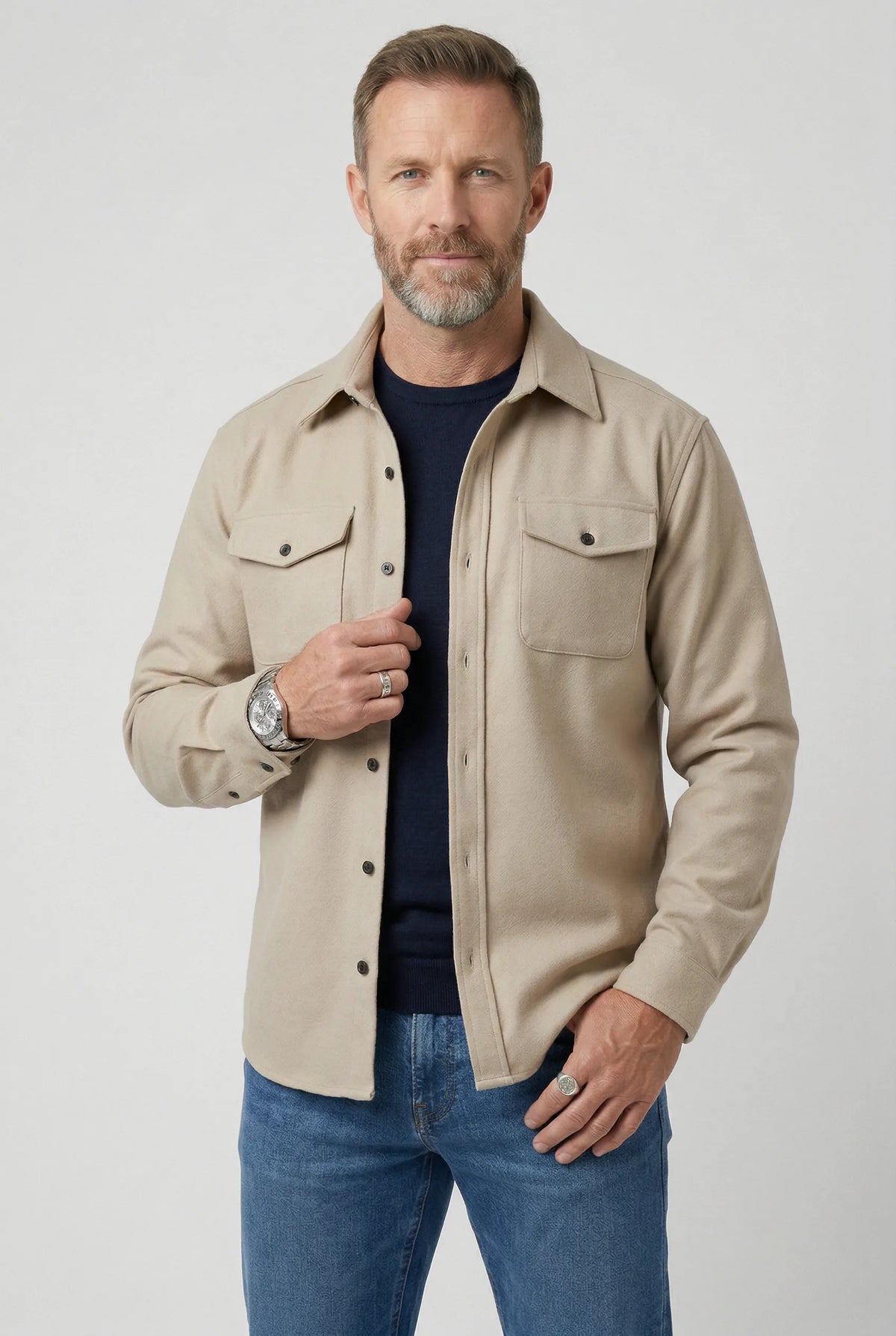 Man wearing a beige brushed overshirt buttoned over a navy T-shirt and denim trousers