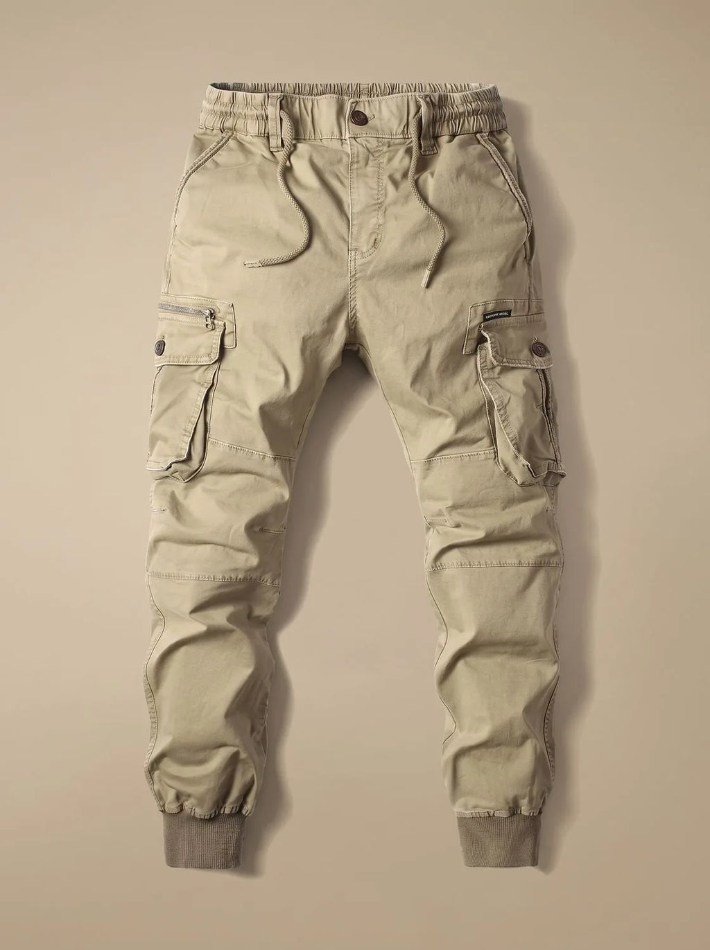 Flat lay of beige cargo joggers with drawstring waist, ribbed cuffs and buttoned flap pockets