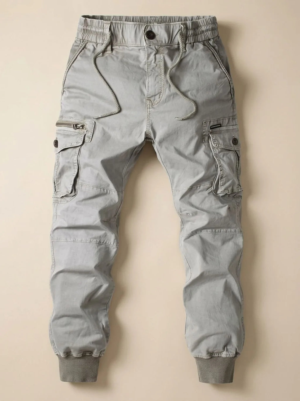 Flat lay of light grey cargo joggers showing side cargo pockets with zip and button fastening