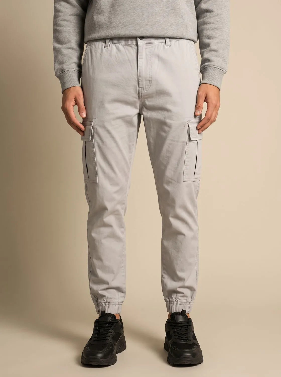 Close-up front view of a man wearing light grey cargo joggers with visible drawstring waistband and cuffed hem