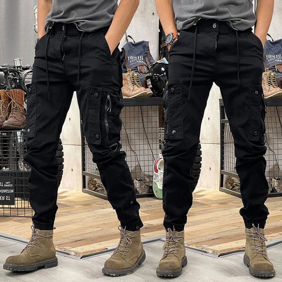 Front and rear view of black cargo trousers with tapered leg, multiple pockets and adjustable ankle straps