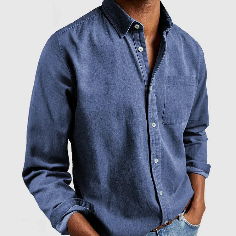 Man wearing a mid-blue denim long sleeve shirt with classic collar and buttoned cuffs, hand in pocket
