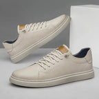 Side profile of off-white faux leather trainer with lace-up front, ribbed sole and tan brand tab on the heel