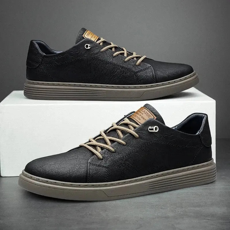 Pair of black faux leather lace-up trainers with contrast taupe laces resting on a white box