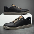 Pair of black faux leather lace-up trainers with contrast taupe laces resting on a white box