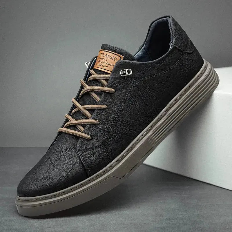 Close angled view of black faux leather trainer showing textured grain, stitched toe panel and chunky grey sole