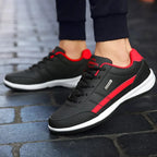 Side view of black trainer with red stripe detail and red ankle trim worn with navy trousers on cobbled street