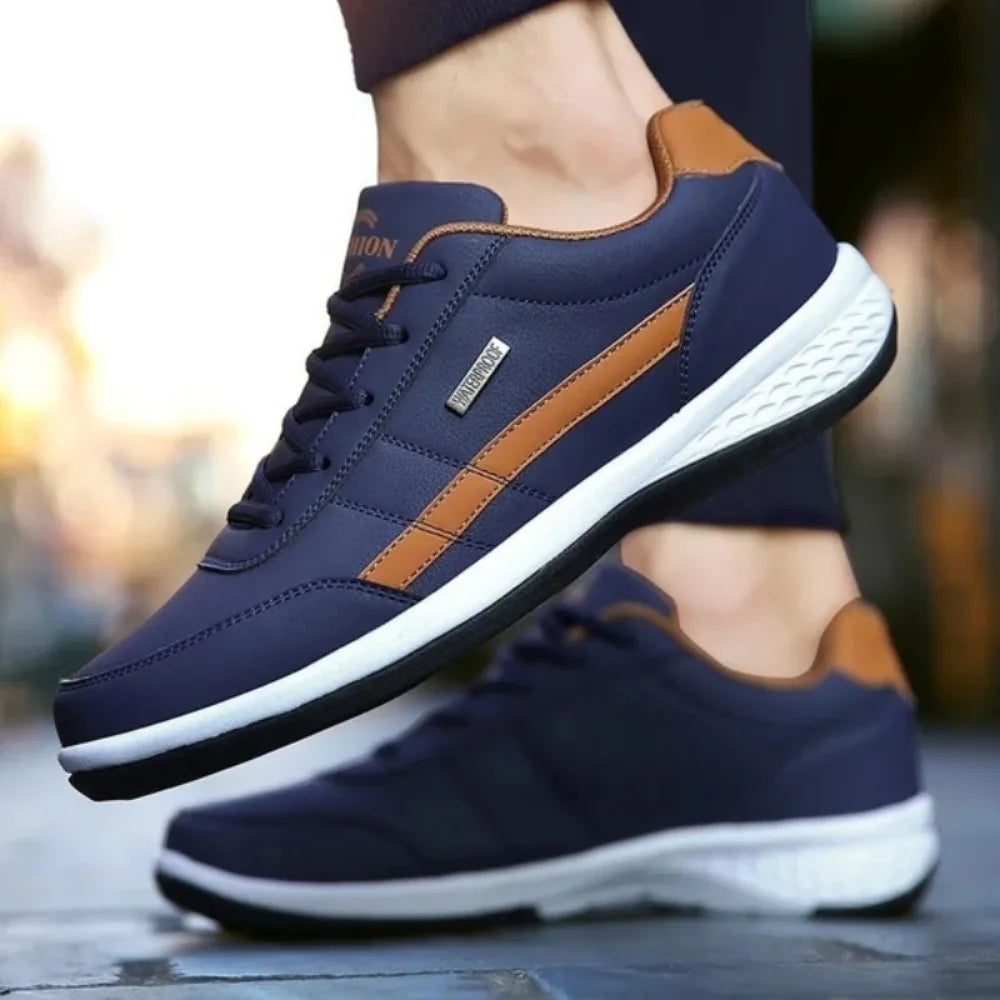 Side profile of navy blue trainer with tan stripe and tan heel trim worn on foot against blurred street background