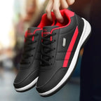 Pair of black trainers with red stripes and red lining held together by hand, showing white midsole