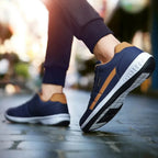 Close-up of feet in motion wearing navy trainers with tan accents and white sole on a stone-paved street