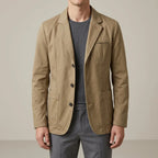 Front view of a man wearing a khaki cotton blazer over a grey t-shirt, unbuttoned collar and notch lapel visible