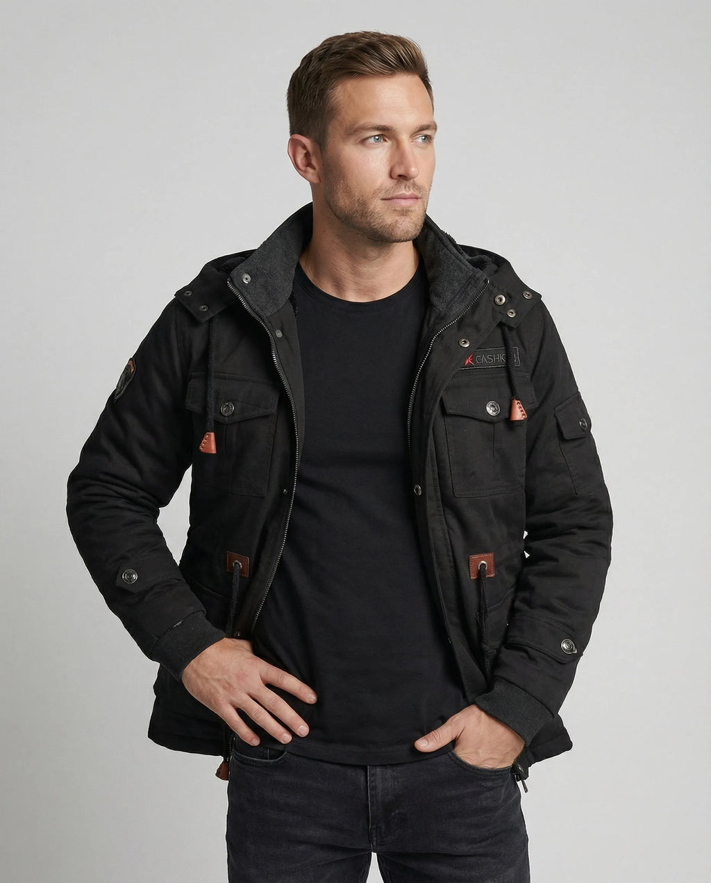 Front view of a man wearing a black multi-pocket cotton field jacket open over a black t-shirt and dark jeans