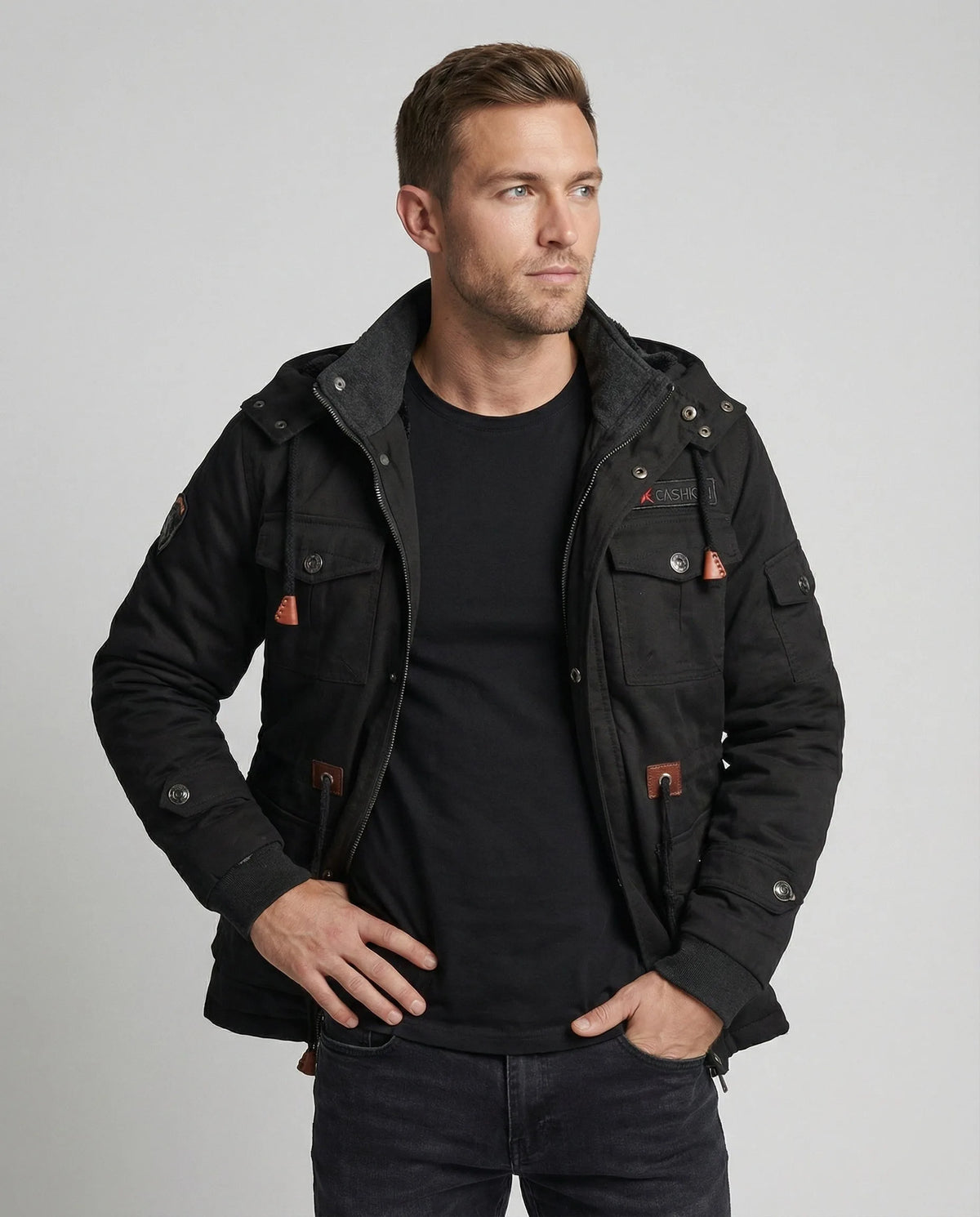 Front view of a man wearing a black multi-pocket cotton field jacket open over a black t-shirt and dark jeans